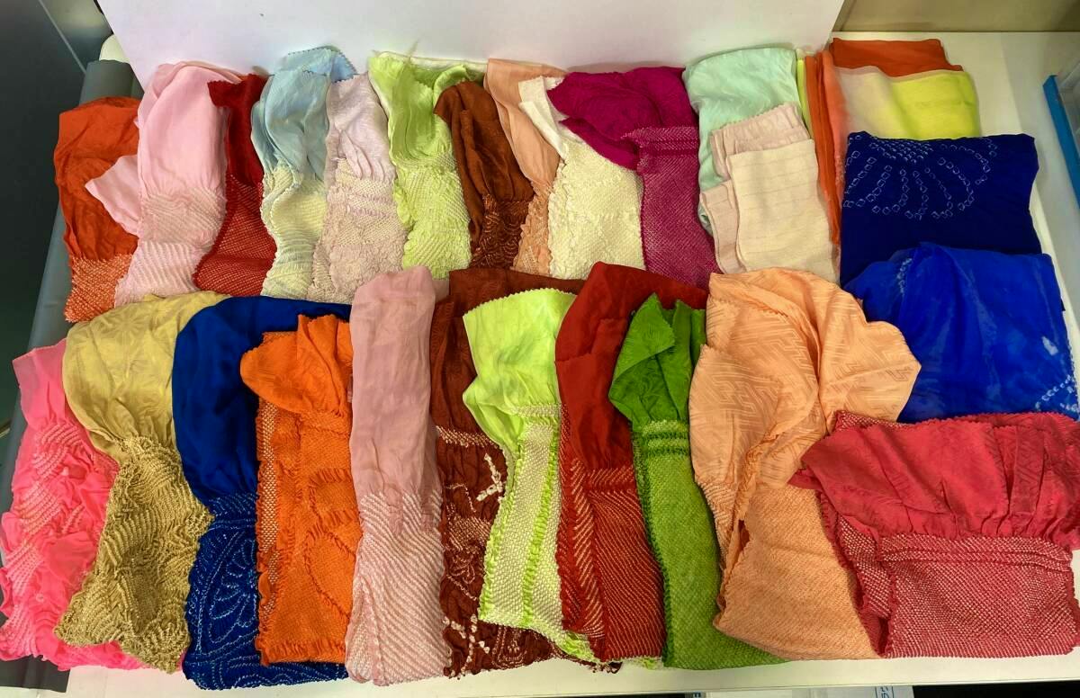 Assorted colorful folded obi-age (obi accessories) pieces laid out in rows on a table, showing many different fabrics and colors.