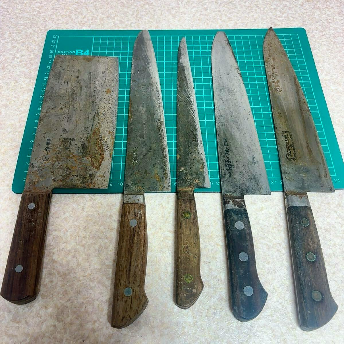 Five worn kitchen/chef knives with wooden handles laid side-by-side on a green cutting mat.