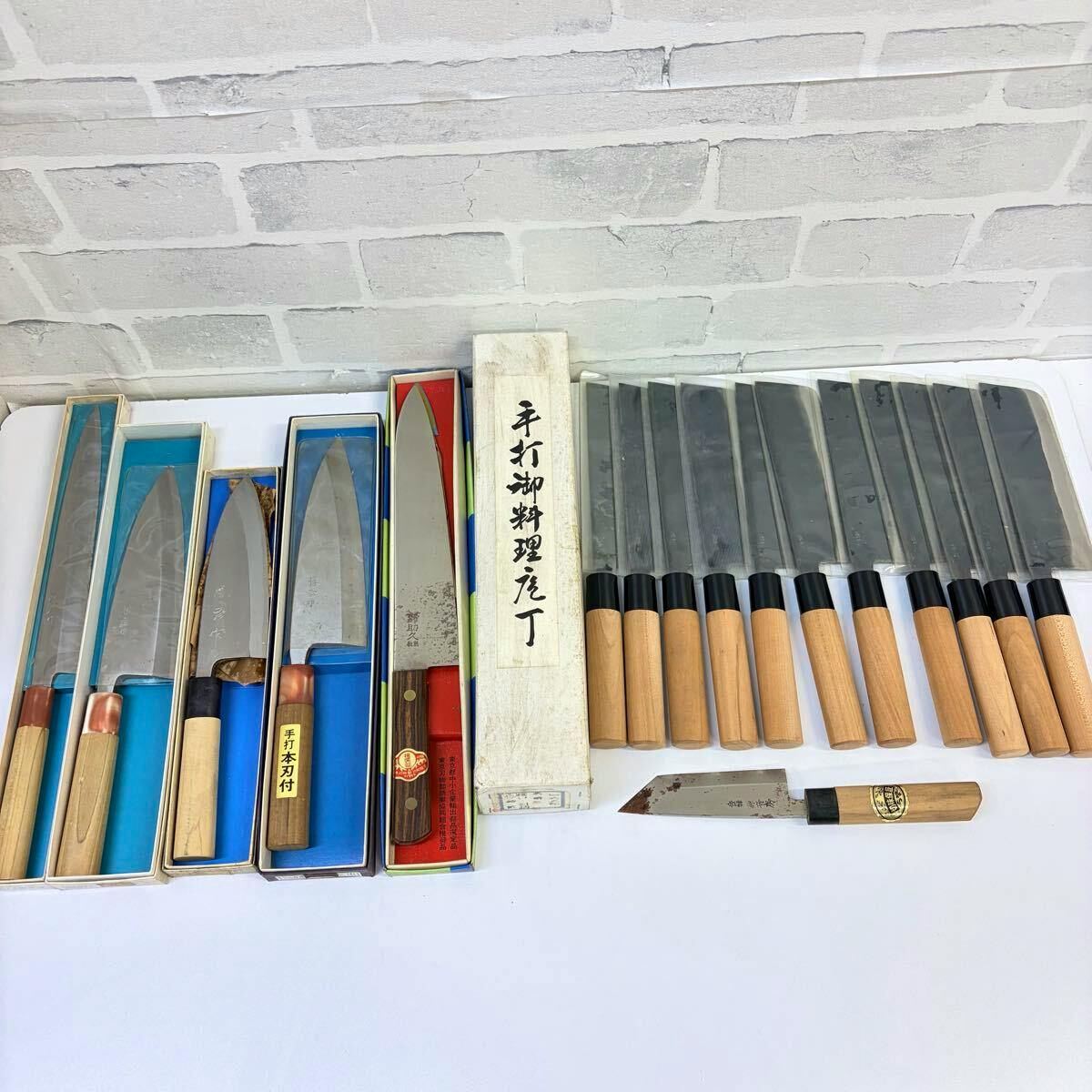 A selection of Japanese chef knives with wooden handles and some in boxes, arranged on a white surface against a light brick-patterned backdrop.