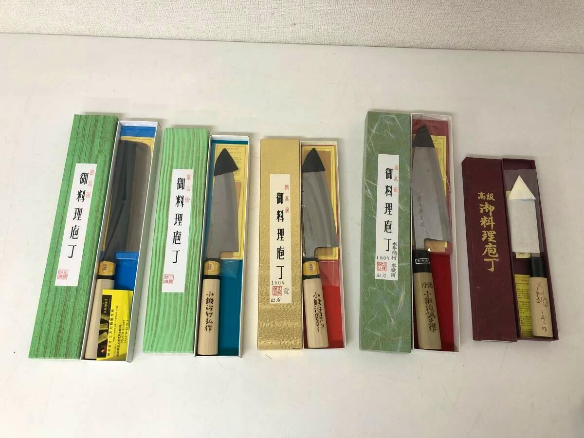 Five chef knives in their boxes laid out side by side on a tabletop.
