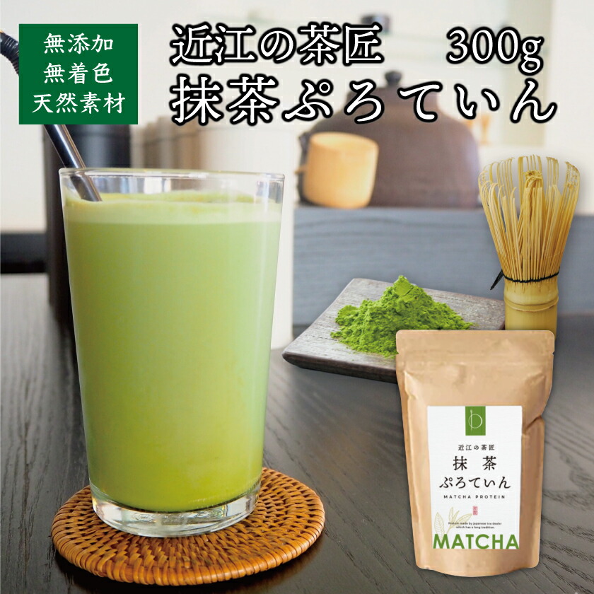 A glass of green matcha protein drink beside a plate of matcha powder, a bamboo whisk, and a standing pouch of matcha protein powder.