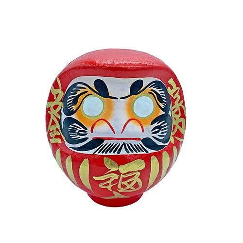 Front view of a red daruma figure showing painted facial features and gold kanji decoration.
