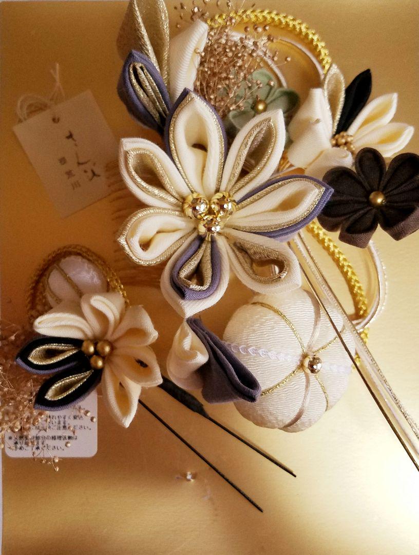 Two-piece kanzashi hair accessory set with white and gold fabric flowers and decorative cords displayed on a gold background.