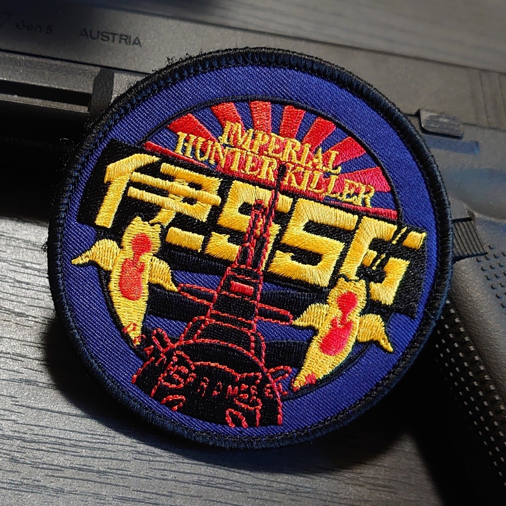 Photograph of a round embroidered 伊556 military patch showing yellow Japanese characters, a red submarine graphic and the text “IMPERIAL HUNTER KILLER” on a blue background.