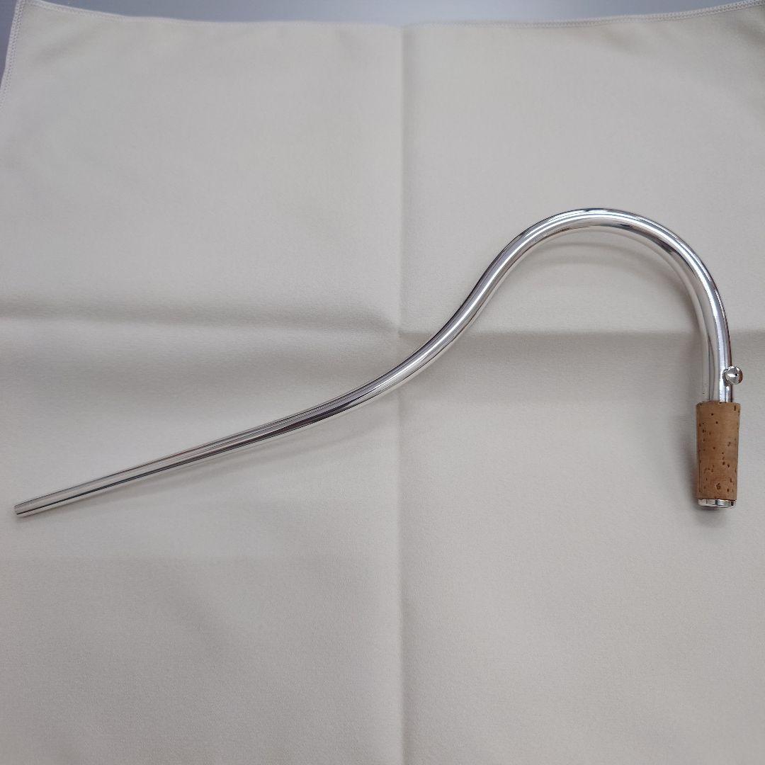 A silver curved bassoon bocal with a cork tenon on a light cloth background.
