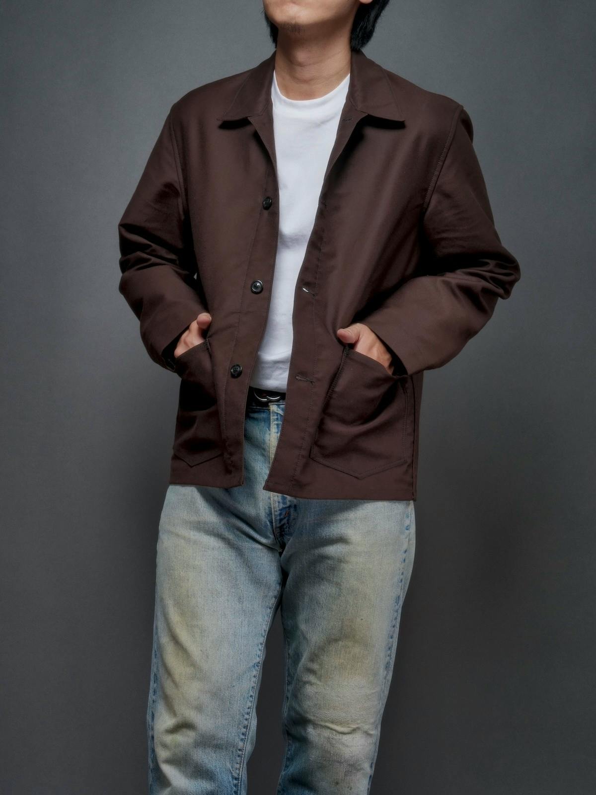 Model wearing the Jean Laumet brown moleskin French worker jacket with hands in the front pockets.