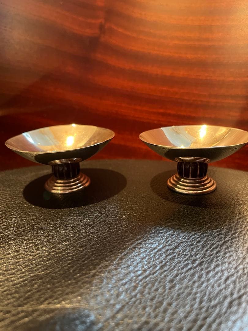 Two sterling silver pedestal dishes displayed on a black surface with a wooden background.