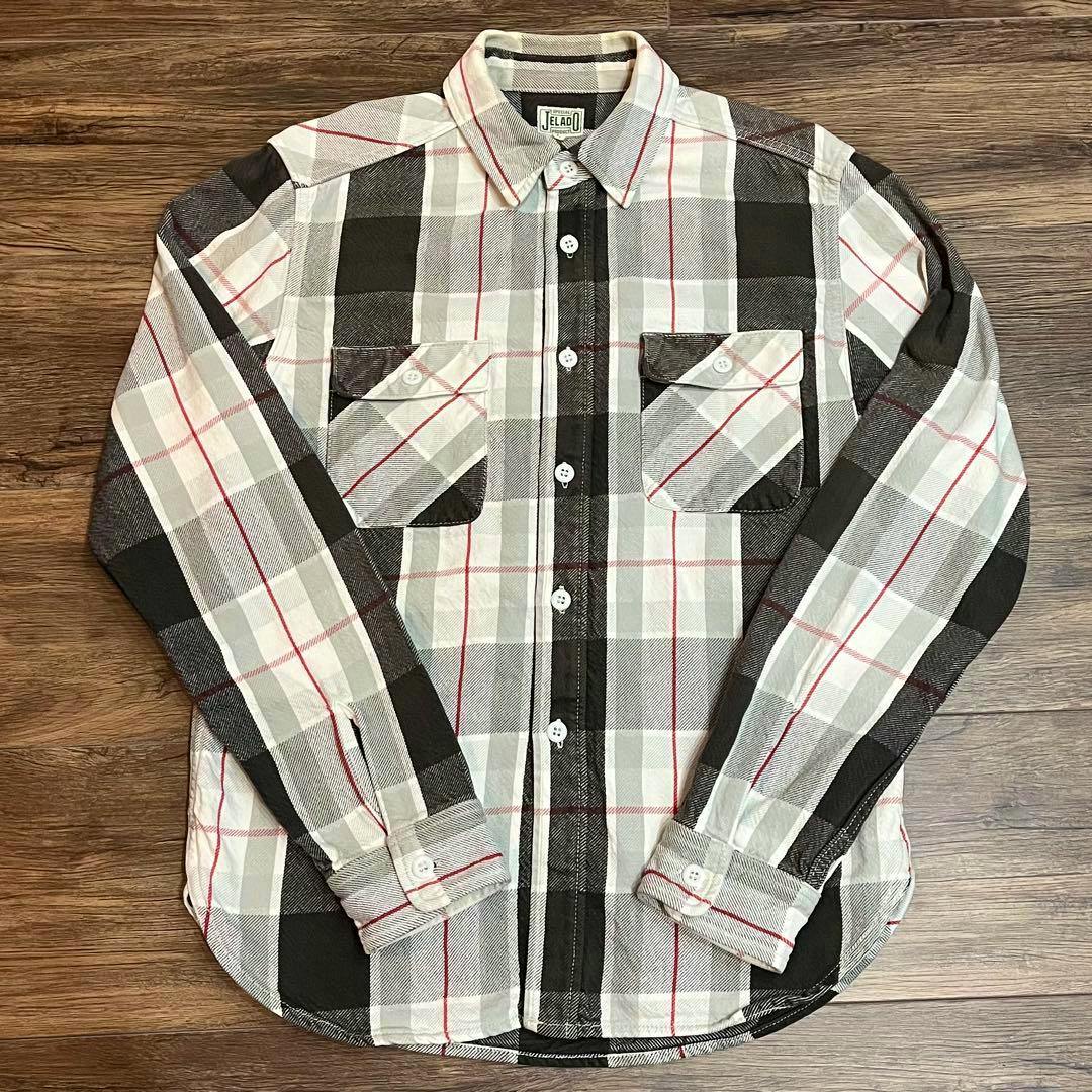 Front view of a JELADO men's heavy flannel cotton shirt (size L) laid flat on a wooden surface, showing the plaid pattern, chest pockets, and buttons.