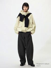 A model wearing black jersey barrel pants with a cream jacket and a dark sweater draped over the shoulders.