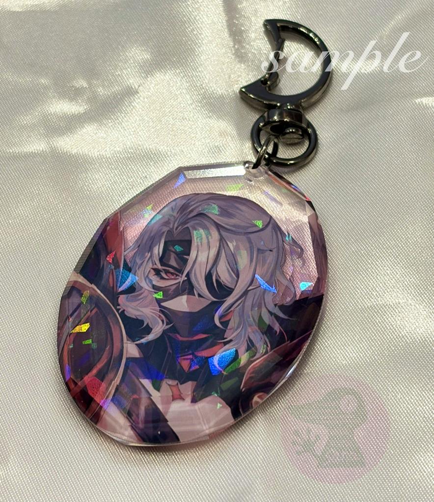 Faceted gem-shaped acrylic keychain showing printed character art and a metal clasp against a satin background.