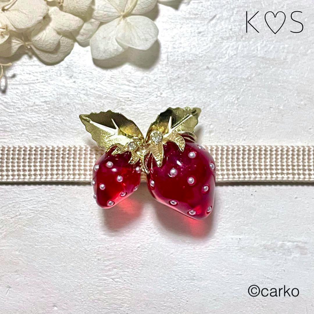 Red strawberry-shaped alloy waist buckle with gold leaves and small round white accents shown on a beige obi strap.