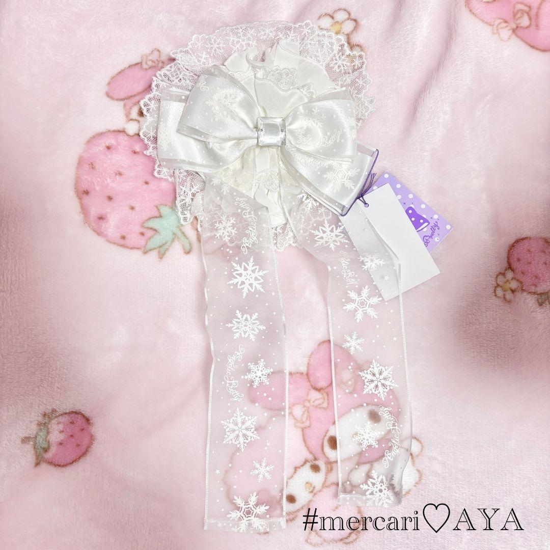 White polyester ribbon hair accessory with lace and snowflake-printed trailing ribbons on a pink blanket.