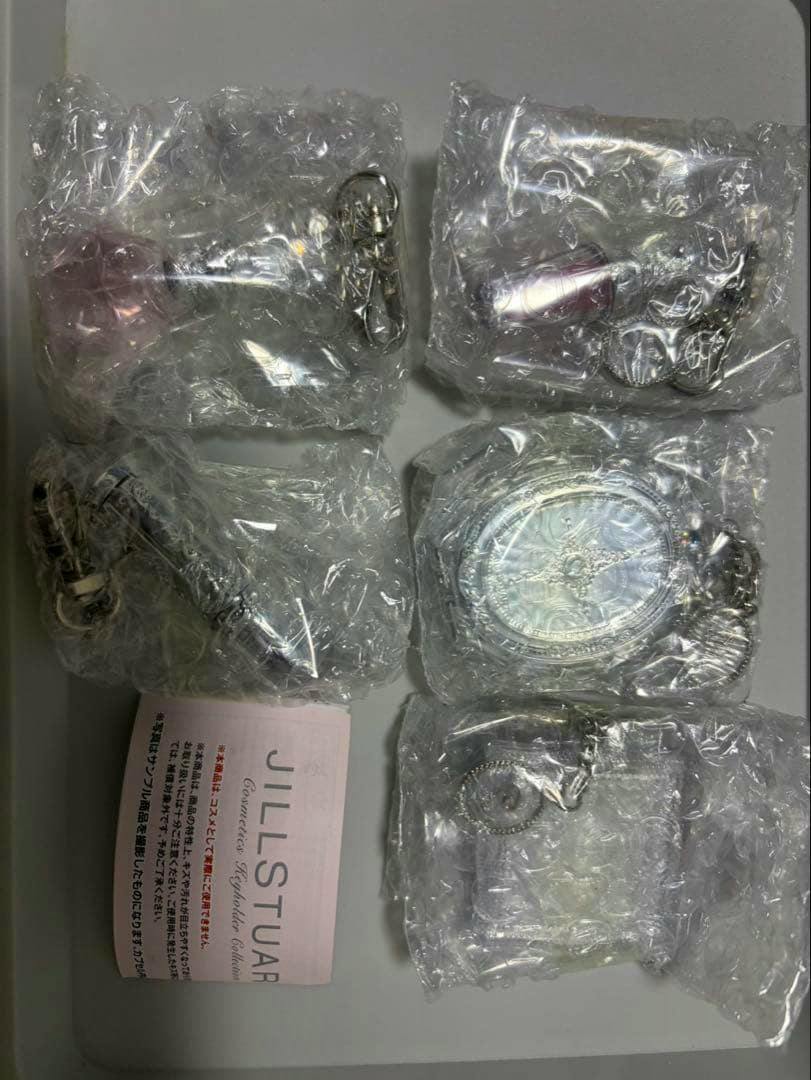 Photo of five Jill Stuart keychain charms individually wrapped in bubble wrap laid on a flat surface with a Jill Stuart insert.