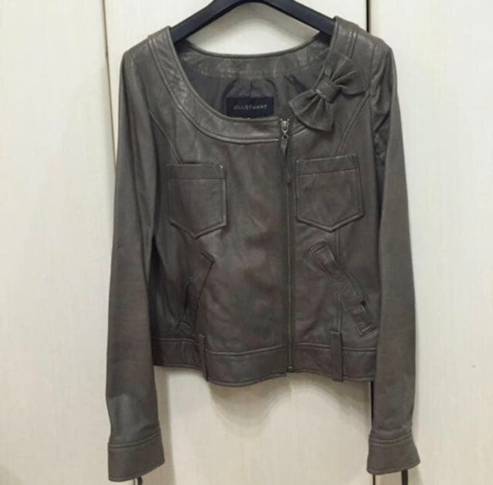 Front view of the lambskin no-collar rider jacket with a front zipper and bow detail, hanging on a hanger.