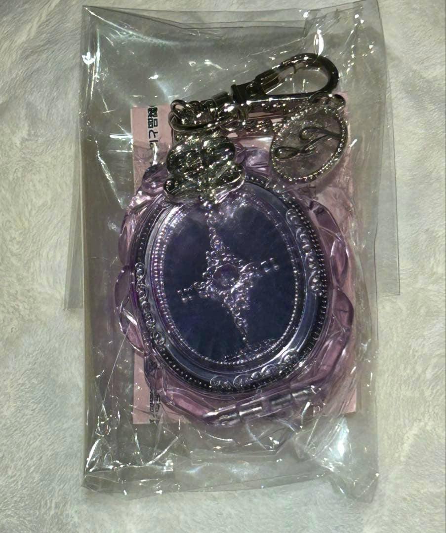 Photo of the JILLSTUART 20th anniversary acrylic keychain mirror in purple inside clear plastic packaging, showing the oval mirror and metal clasp.