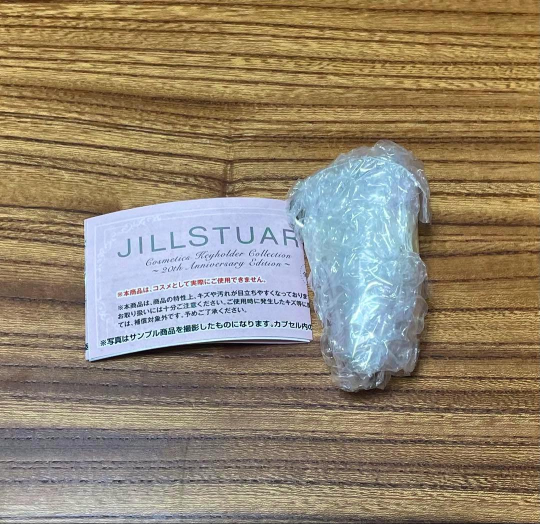 Photograph of a JILLSTUART cosmetics keychain wrapped in bubble wrap next to a JILLSTUART instruction leaflet on a wooden surface.