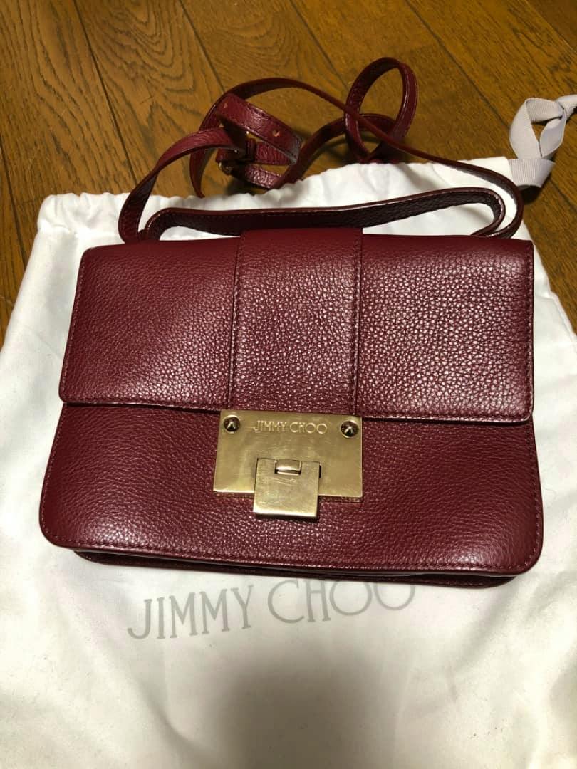 Burgundy Jimmy Choo cow leather shoulder bag with gold clasp resting on a white dust bag.