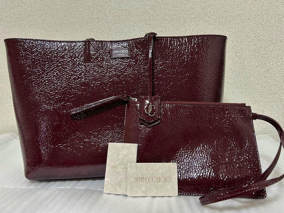 Patent leather Jimmy Choo tote bag with matching pouch and two cards displayed on a surface.