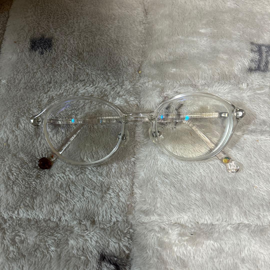 Clear round eyeglasses with corrective lenses resting on a gray plush surface.