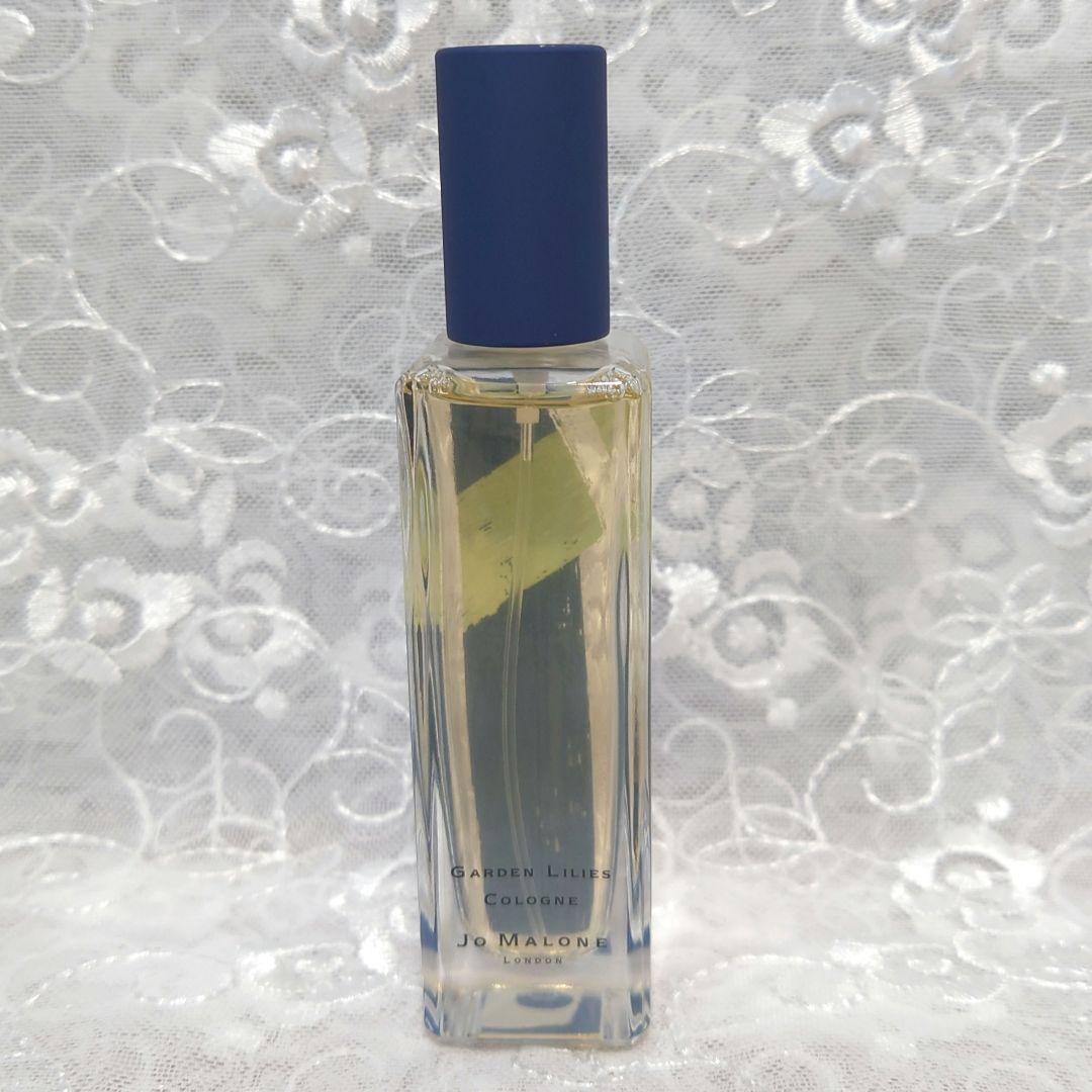Glass bottle of Jo Malone Garden Lilies cologne (30ml) with a blue cap standing against a lace background.