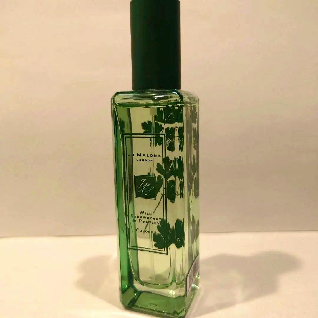 A green Jo Malone "Wild Strawberry & Parsley" cologne bottle with a black cap and parsley leaf design on a plain background.