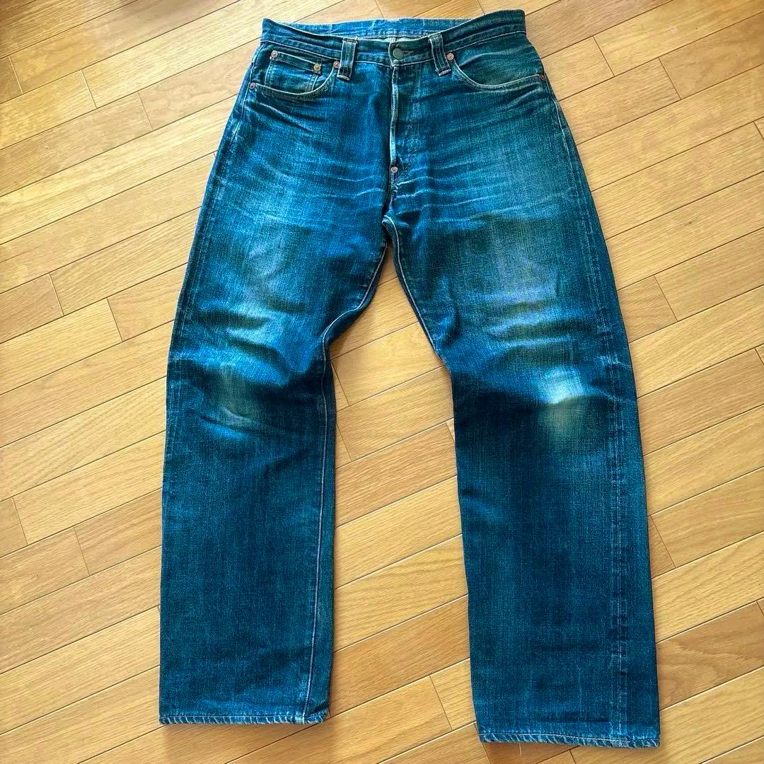 Front view of men's blue denim jeans laid flat on a wooden floor.