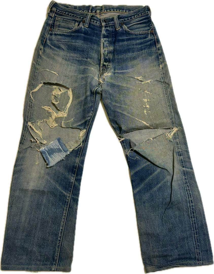Front view of men's denim jeans showing heavy wear, large knee rips, and a faded blue wash.