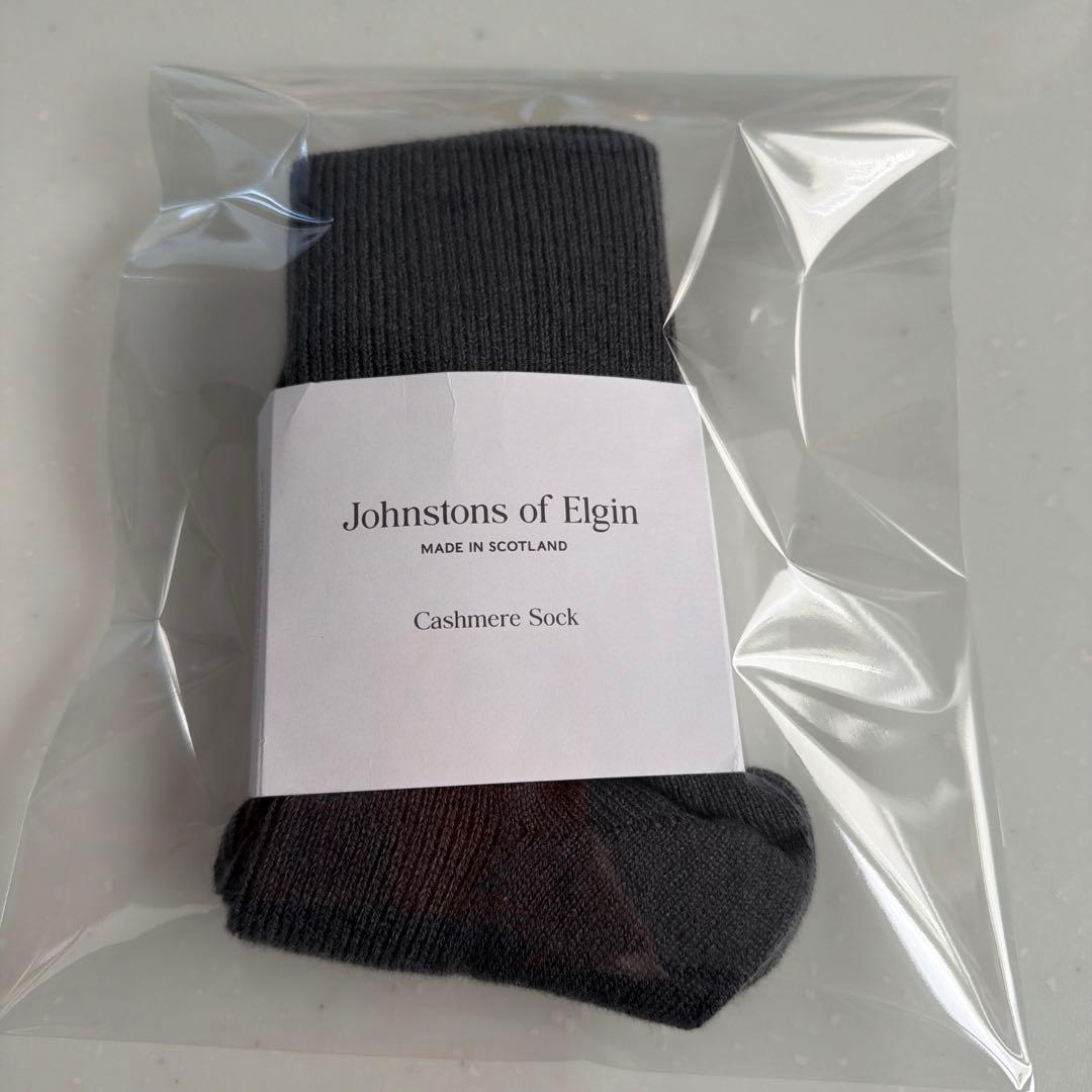 A folded dark cashmere sock by Johnstons of Elgin in clear plastic packaging with the brand label visible.