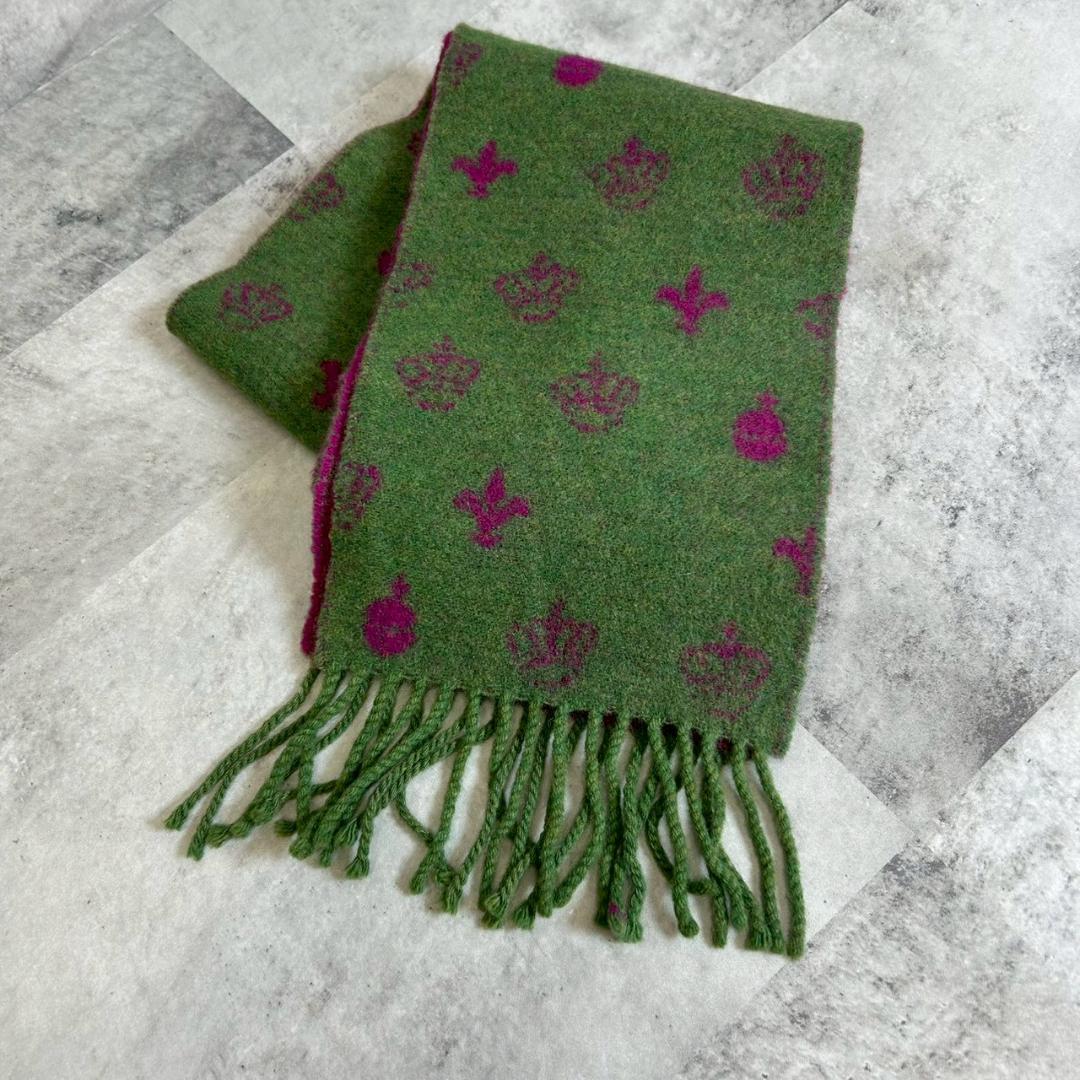 Green wool scarf with purple repeating motifs and twisted fringe, folded on a gray surface.