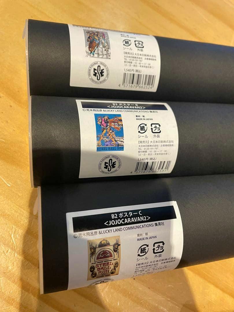 Three rolled B2 Steel Ball Run (JoJo) posters with product labels and barcodes visible on a wooden surface.
