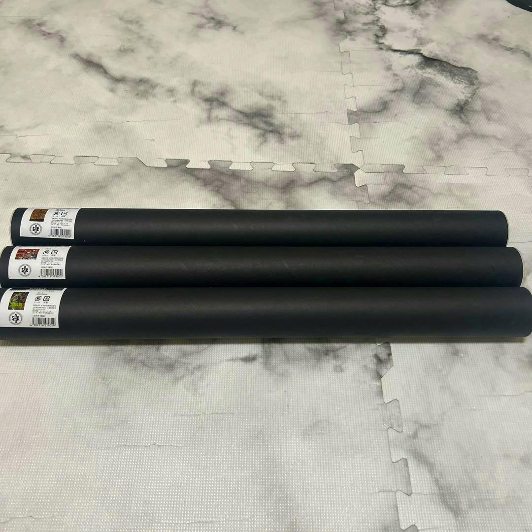 Three rolled posters in black tubes with JoJOCARAVAN product labels laid on a marbled floor.