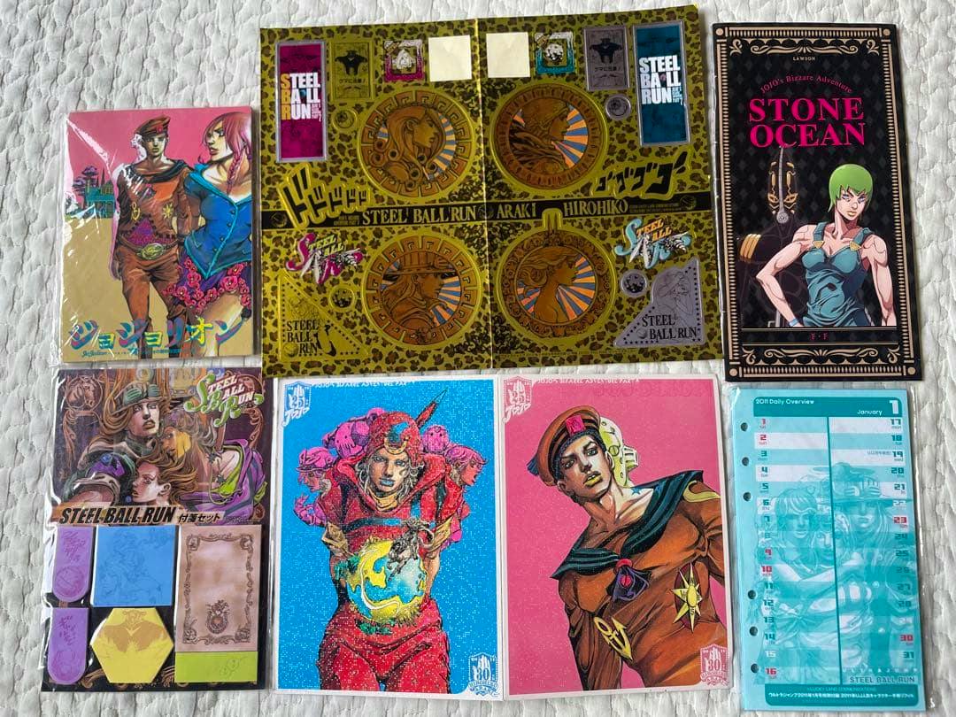 A JoJo's Bizarre Adventure postcard set showing multiple illustrated postcards and paper goods arranged on a white quilted surface.
