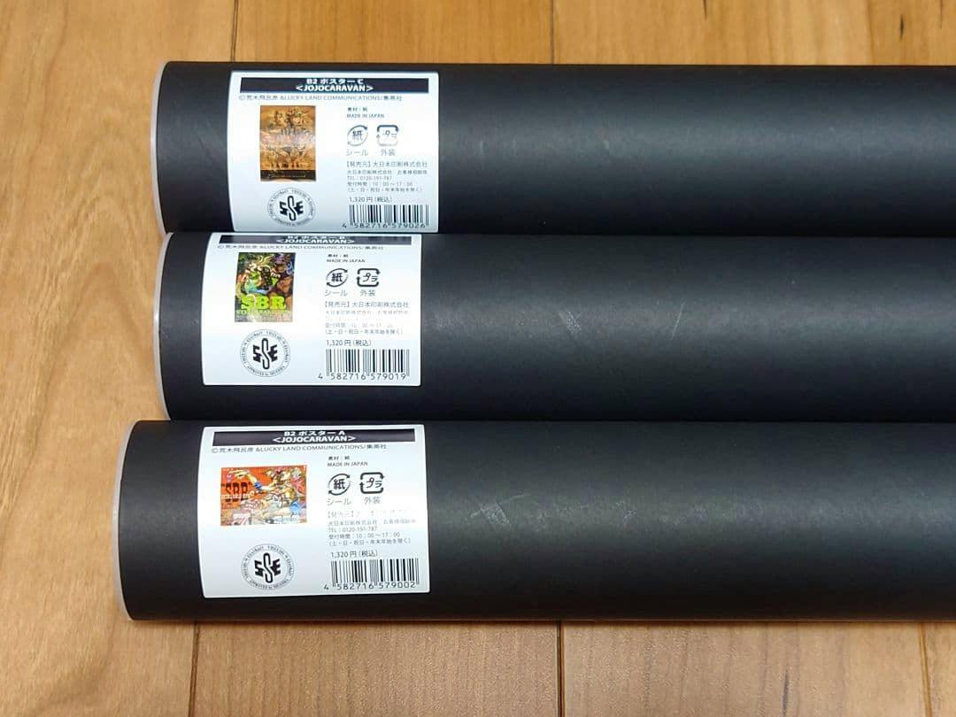 Three rolled B2 posters from the JoJo Caravan set with white product labels shown on a wooden floor.