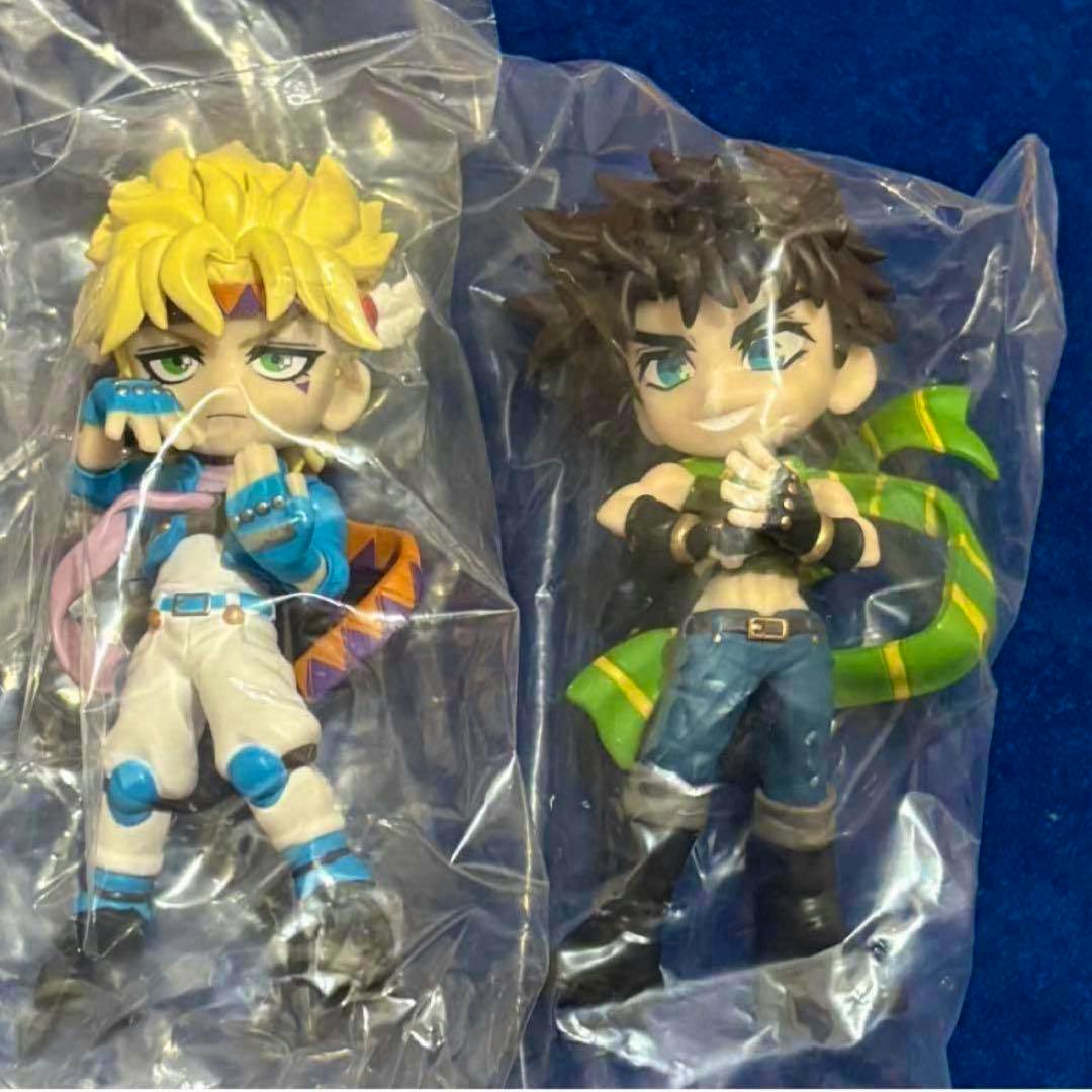 Two JoJo's Bizarre Adventure plastic figures (Joseph and Caesar) sealed in clear bags on a blue background.
