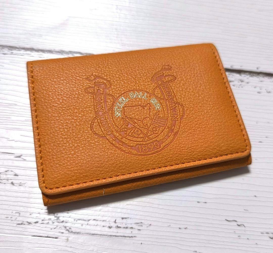 Orange card holder (JoJo's Bizarre Adventure: Steel Ball Run) with an embossed circular emblem on the front, shown on a white wood background.