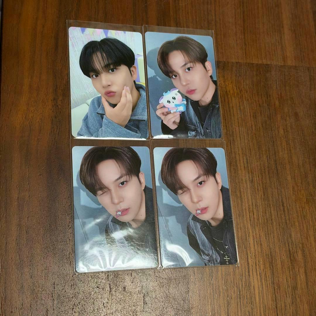 Four glossy rectangular photocards showing a young man, arranged in a 2x2 grid on a wooden surface.