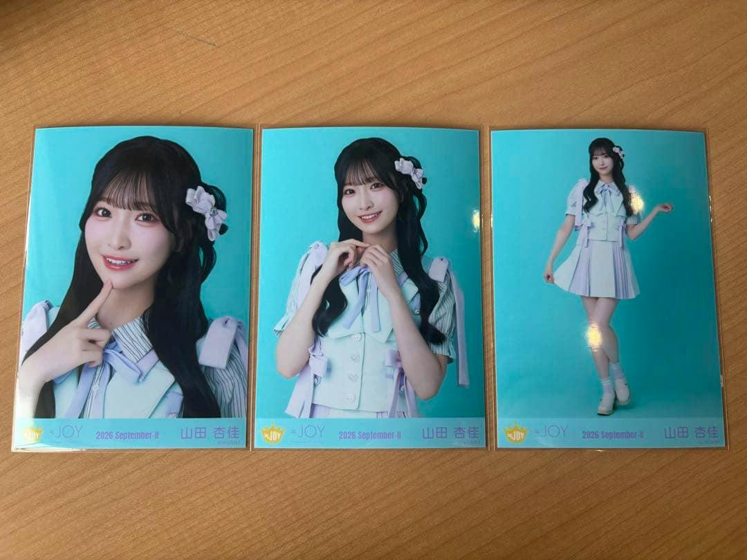 Three glossy photo cards showing a woman with twin-tail hairstyle in a light blue singing outfit on a teal background, laid on a wooden surface.