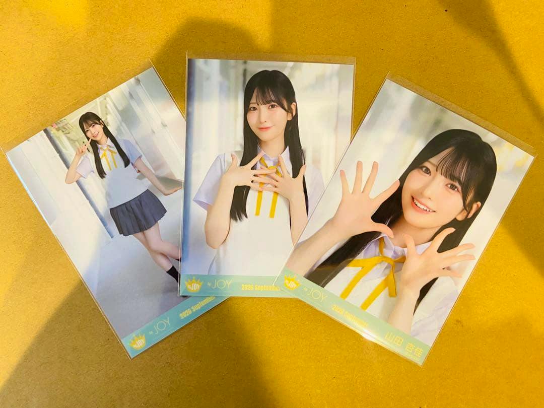 Three glossy photocards laid flat on a yellow surface showing a woman in a white blouse and yellow ribbon MV costume.