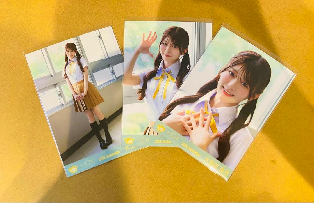 Three printed photocard-style photographs of a woman wearing a school-uniform MV costume arranged on a yellow surface.