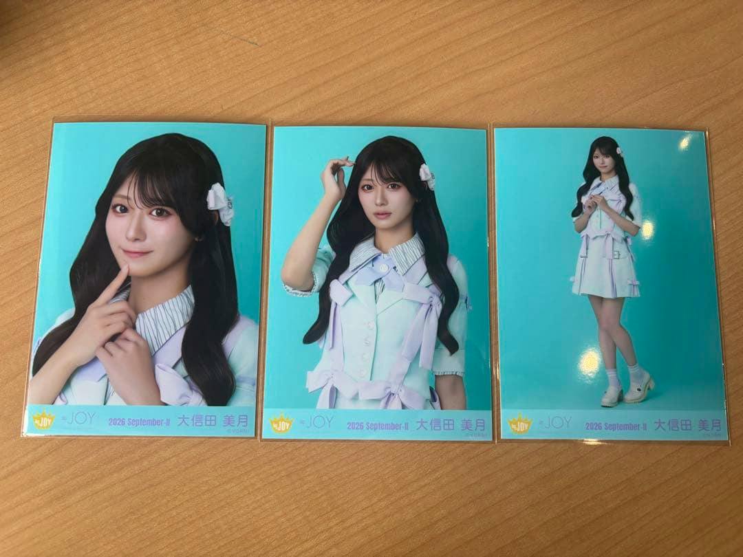 Three collectible photo cards showing a woman in a light-colored singing costume with twin-tail hairstyle displayed on a wooden surface.
