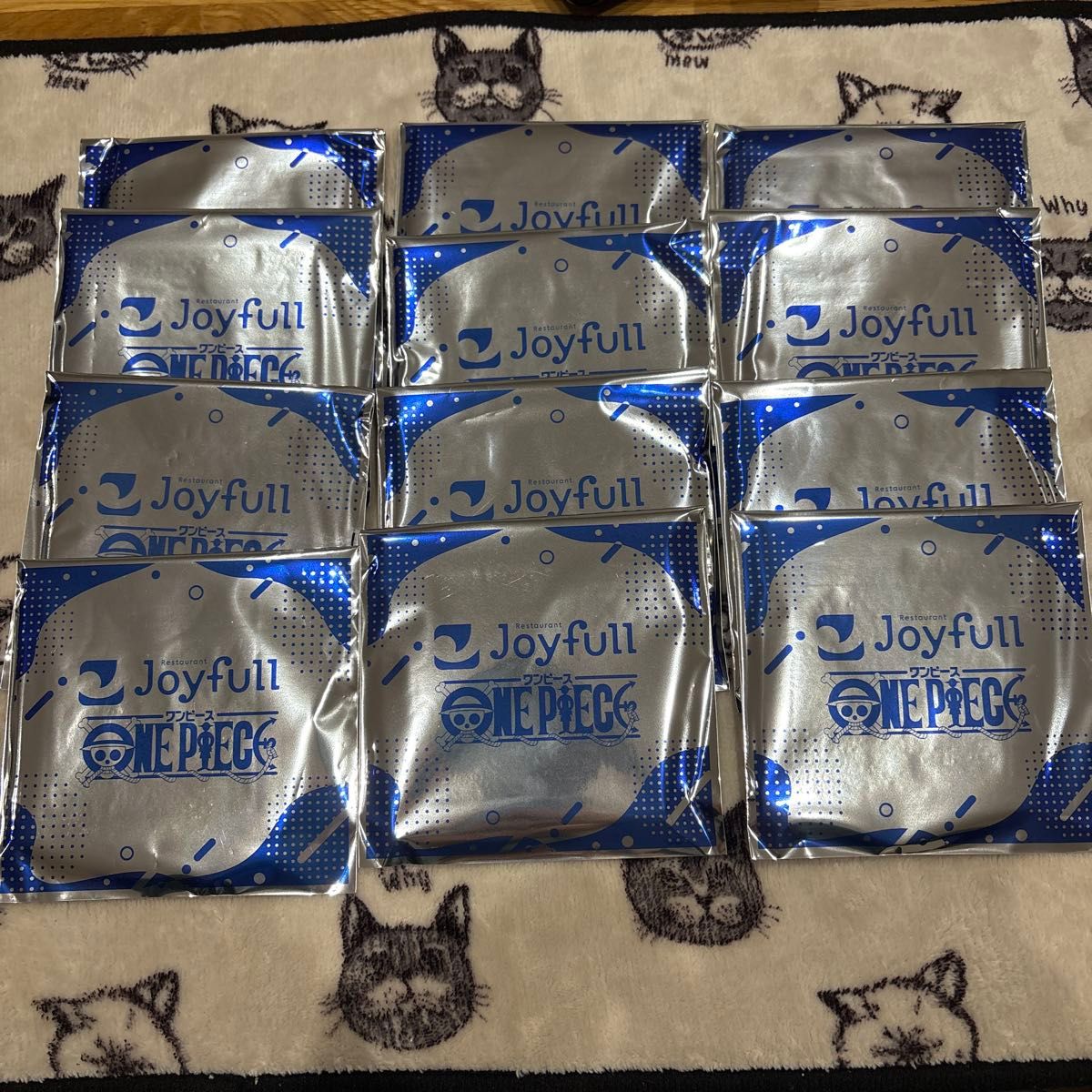 Twelve unopened Joyfull One Piece cork coaster packages arranged on a blanket.