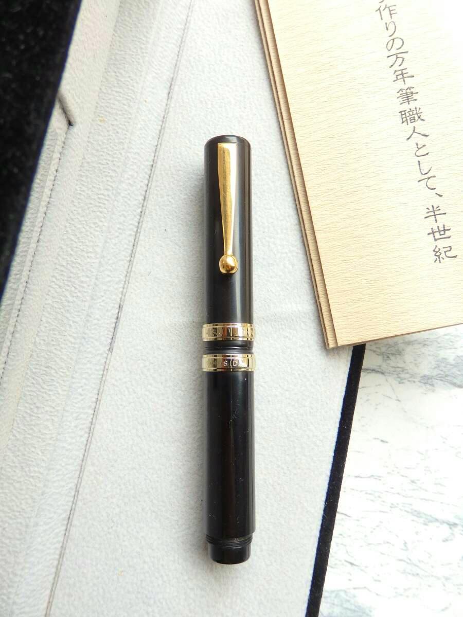 Capped black lacquered fountain pen with a gold clip and two gold bands, shown on a light textured surface next to a booklet.