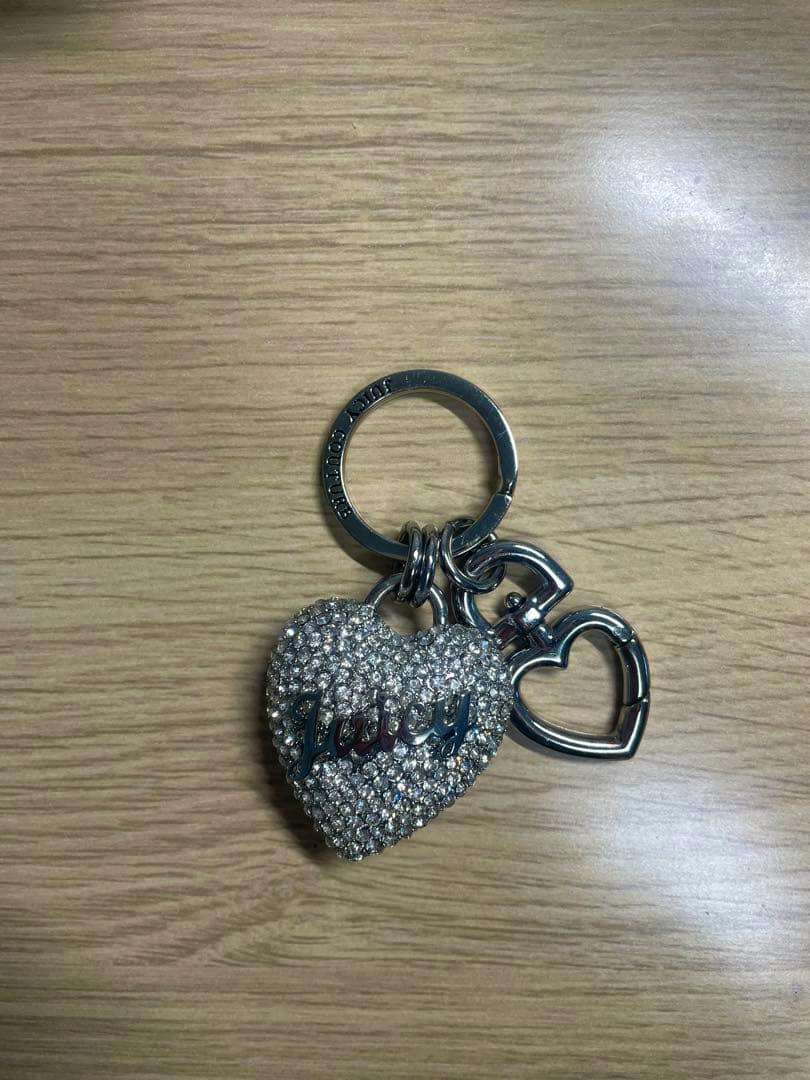 Juicy Couture heart-shaped silver bag charm with rhinestones and ring placed on a wooden surface.