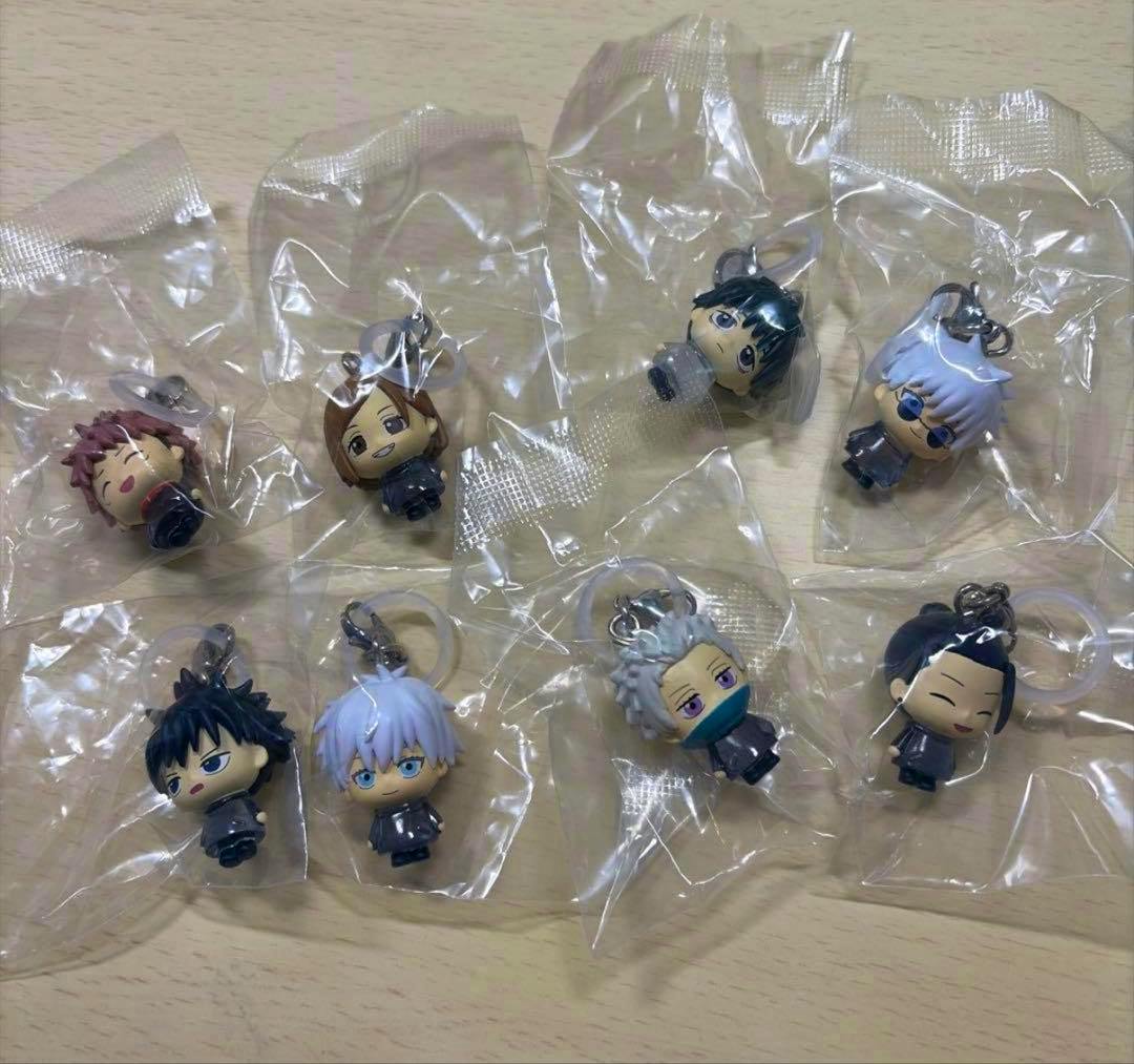 Photo of eight Jujutsu Kaisen 5th anniversary small plastic keychain figure accessories, each sealed in individual clear plastic bags on a tabletop.
