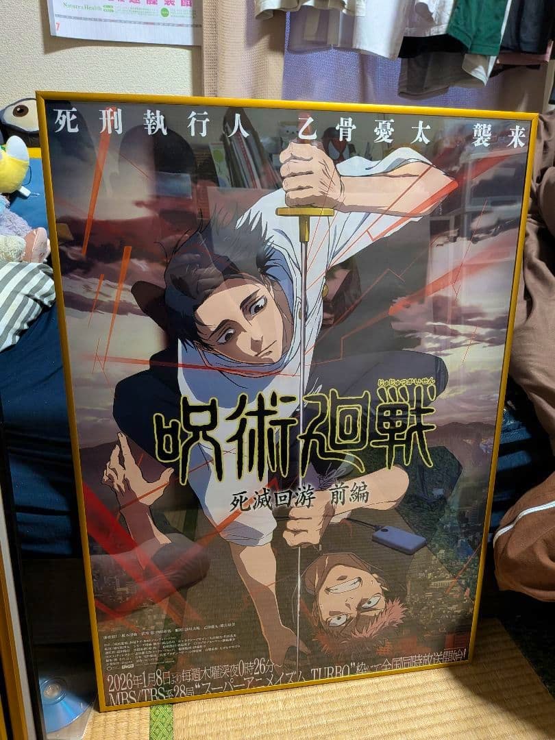 Framed B2 poster for 呪術廻戦 死滅回遊 前編 showing two characters and the Japanese title, photographed leaning against a wall in a room.