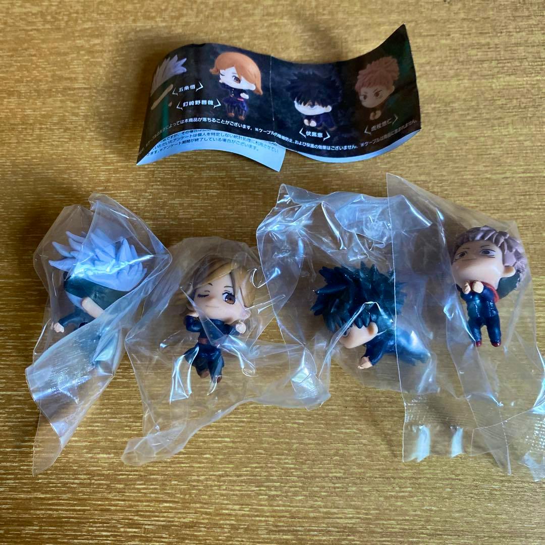 Four Jujutsu Kaisen Hugcot mini figures in individual plastic bags with a paper insert on a gold surface.