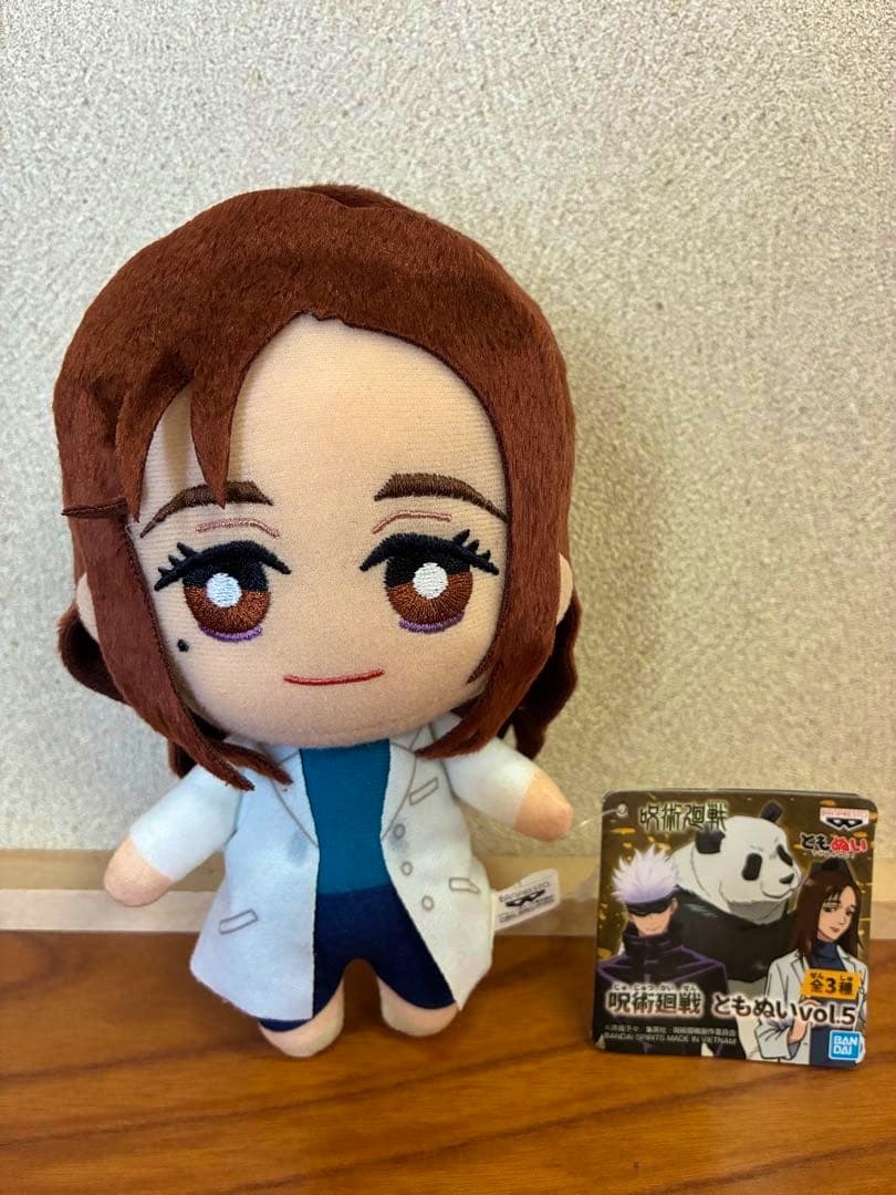 Front view of the plush from "Jujutsu Kaisen" Tomonui vol.5 (Ieiri Shoko) standing on a wooden surface with its tag box to the right.
