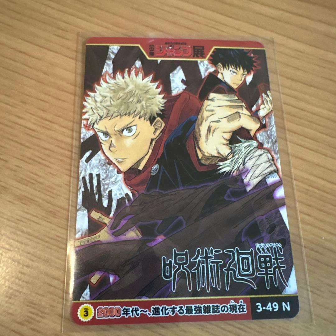 Photocard of Itadori Yuji from Jujutsu Kaisen in a clear protective sleeve resting on a wooden surface.