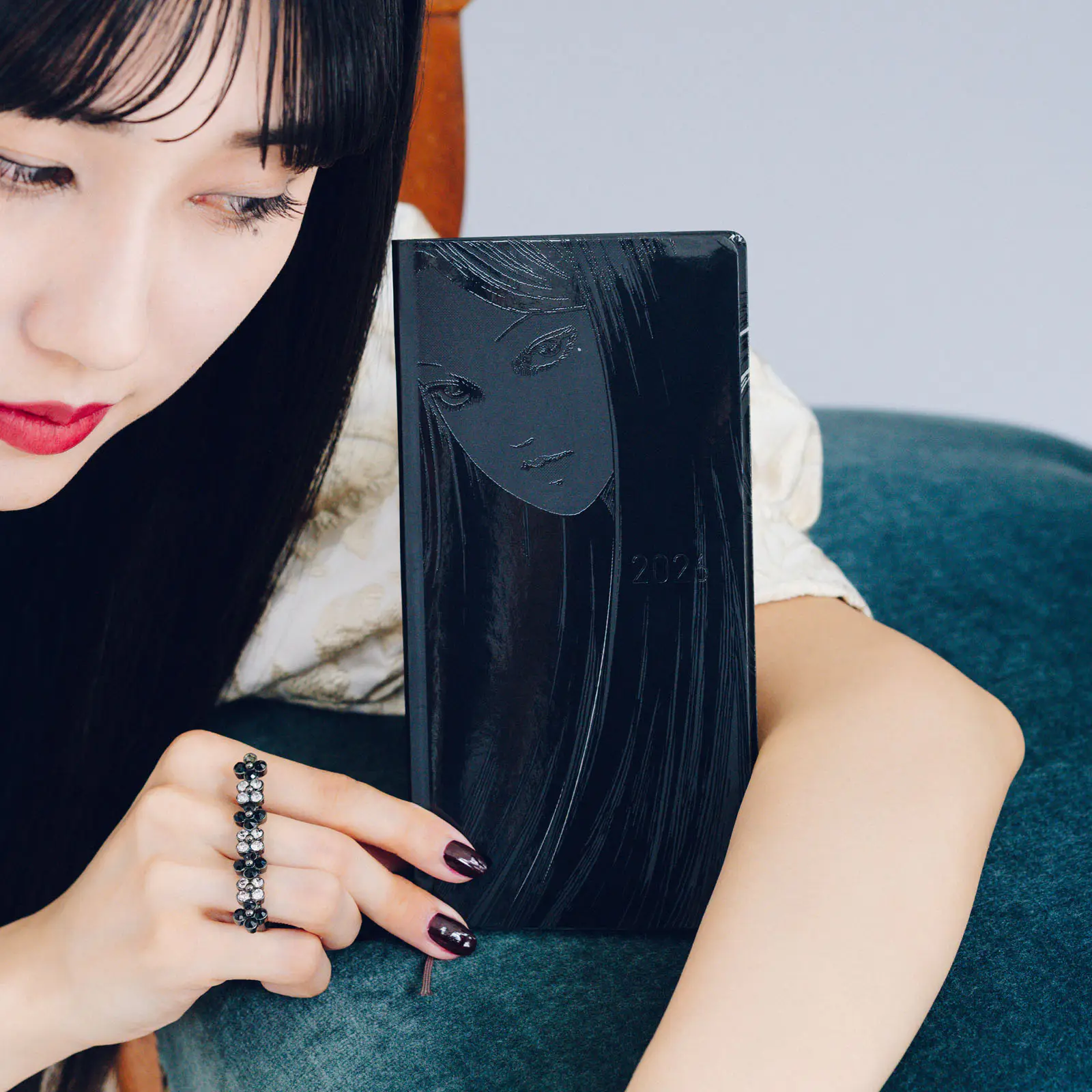 Person holding a black Junji Ito: Tomie hardcover weekly horizontal notebook showing an embossed face on the cover.