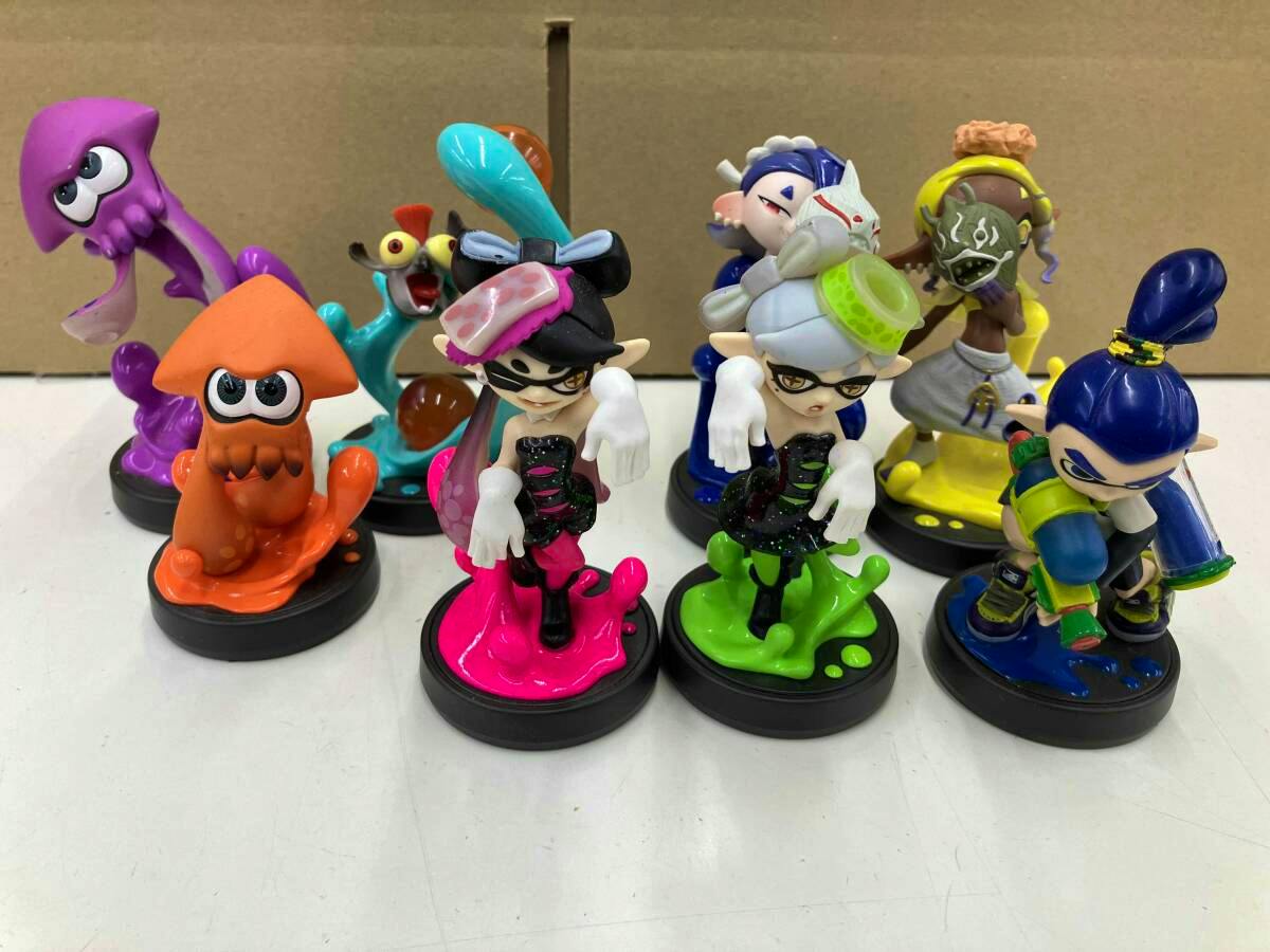 Multiple Splatoon amiibo figures and squid characters displayed on a white surface with a cardboard background.